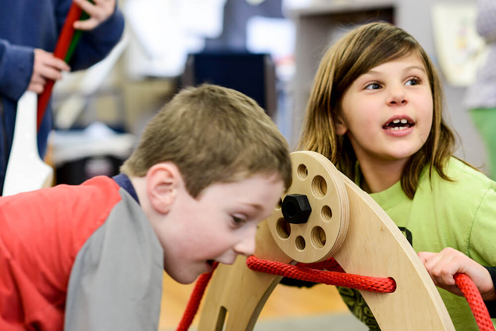 Two children, a boy and a girl, engaged in collaborative play with Rigamajig building materials